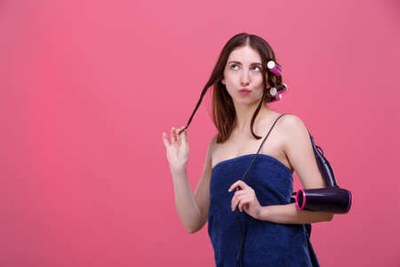 A coquettish girl, in a bath, with hair curlers, squeezed lips, looks up and plays with a curl of hair.の写真素材
