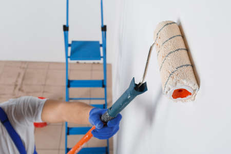 A man in gloves paints a wall with a roller for paint. Close-up. View from above.の写真素材