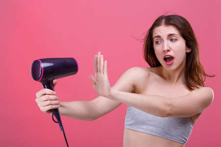 Fearful girl , frightenedly covers hand with a stream of air from the hair dryer that blows on her.の写真素材