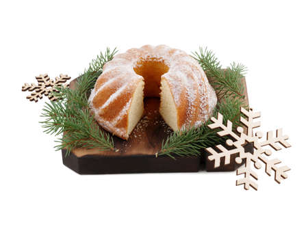 Delicious Christmas cake sprinkled with powdered sugar and with a cut piece on a wooden board, next...