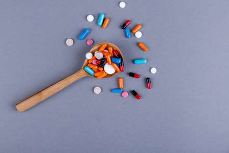 A bunch of different colored pills on a large wooden spoon on a gray background. The concept of...
