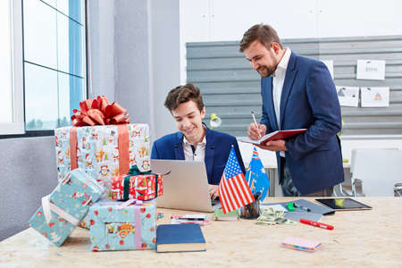 Two office workers behind the work process next to the Christmas gift boxes.