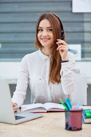 Girl office worker sitting at desk in headphones and with laptop.の写真素材