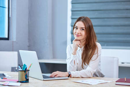 A girl office worker, sitting at table with laptop and smiling.の写真素材