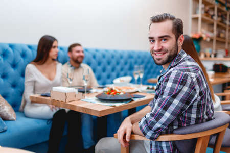 A company of young people spend time in a cafe chatting, and one guy smiles at the camera.の写真素材