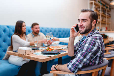 A company of people spend time in the cafes, and one guy is distracted and speaks on the phone.の写真素材