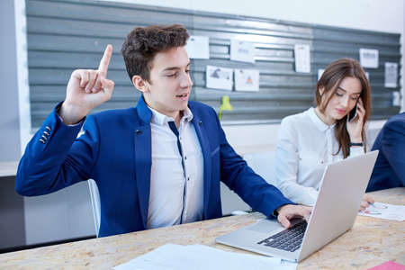 A guy working behind a laptop and lifting his index finger.の写真素材