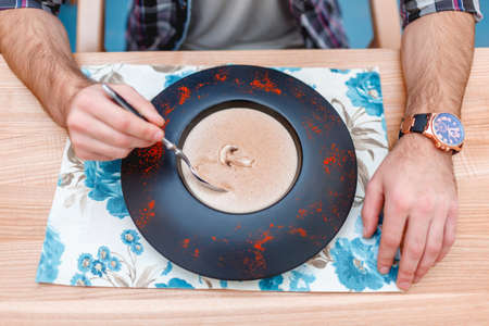 The guy eats a mushroom cream soup from a dark plate. Close-up.の写真素材