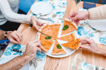 A company of young people simultaneously takes a piece of pizza. Close-up.の写真素材