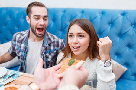The company is sitting in a cafe, someone gives the girl a pizza, the guy in the background laughs.の写真素材