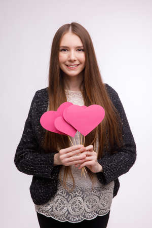 Happy girl, european appearance, holding several paper pink heart on stick and smiling. Isolated .の写真素材