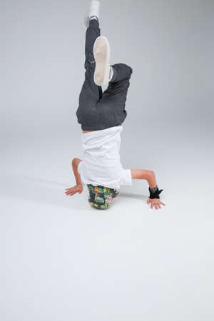 The active boy is a teenager, dancing standing on his head. On a gray background.