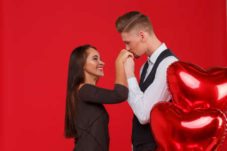 Couple in love, guy kisses a girls hand, next to balls in the shape of a heart. Red background.の写真素材