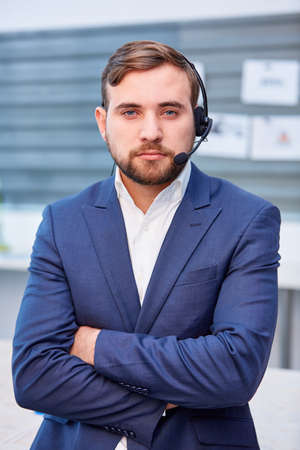 A serious male office worker in headphones stands with his arms crossed over his chest.の写真素材