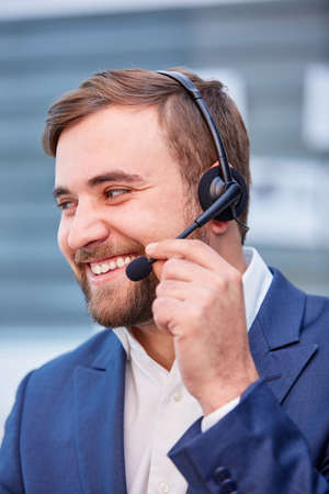 A happy man in headphones on his head, looks away and laughs, adjusting the microphone of the headphones.の写真素材