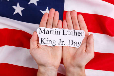 Hands of a man hold the inscription is Martin Luther King Jr. Day against the background of the American flag.の写真素材