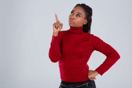 Pensive African American woman with a serious look looking up and showing the index finger up.の写真素材