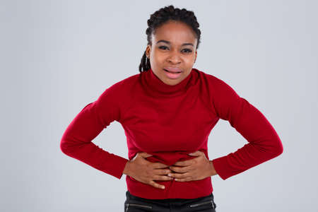 An unhappy African American girl bent over and clings to her belly imitating pain.