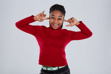 A funny Afro-American girl grimaces a face and puts her fingers in her ears.の写真素材