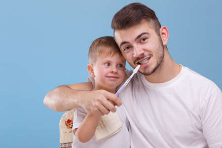 A father with a small son, having fun together, father is teaching his son to brush teeth with a...