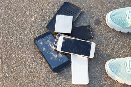 Two smartphones with a broken screen on the asphalt near the mens legs.