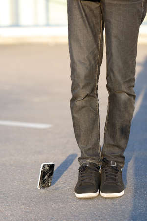 A smartphone with a broken screen falls on the asphalt near the feet of the guy.の写真素材
