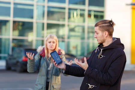 Emotional young guy, holding a mobile phone with a broken screen, sadly gesturing with his hands.の写真素材
