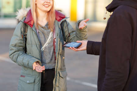 Young girl and boy emotionally communicate and gesturing with hands, the guy holds a broken mobile phone.の写真素材