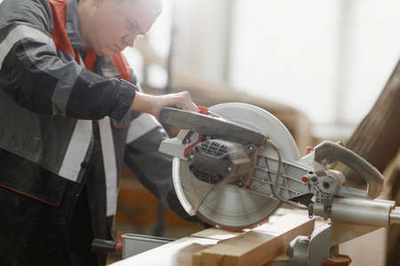 The man is a carpenter, with a serious look, cuts a piece of wood with a lathe. Indoors.の写真素材