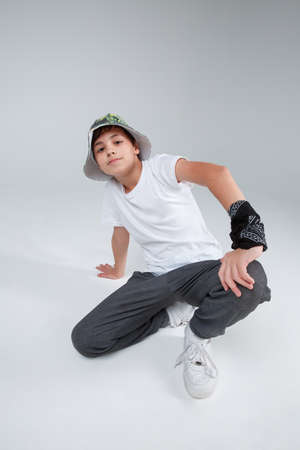 A cute guy teenager, posing squatting, leaning with one hand on the floor.の写真素材