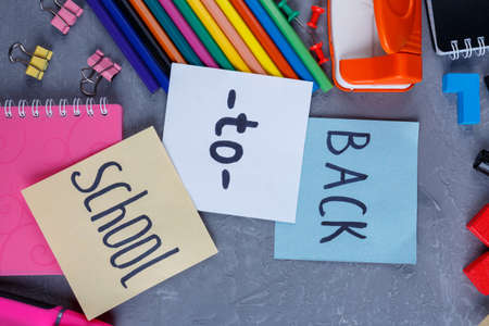 On a dark uneven background, a layout of various color stationery, notebooks and clips and colored leaves with the inscription Back to school. View from above.の写真素材