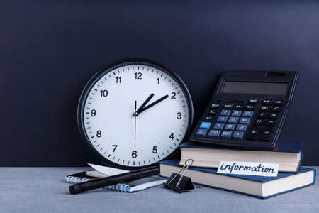 On the table is a tablet with the inscription Information, next to a large round watch, several books, a calculator, a notepad and a clip.の写真素材