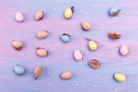 Easter background with colorful quail eggs and feathers. Top view, wooden lavender background. Easter decorations concept.の写真素材