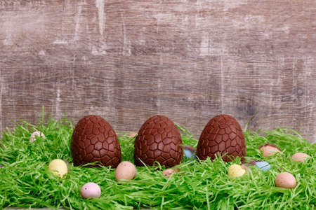 Three chocolate eggs and colorful quail eggs on a green grass in front of a wooden background....