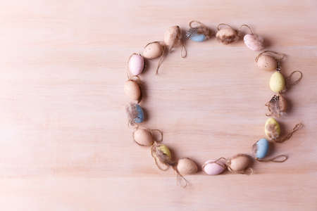 Top view of colorful quail eggs with feathers in circle form on a light wooden background with copy space. Easter holidays conceptの写真素材