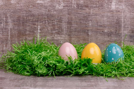 Three bright colorful eggs on a green grass in front of a wooden background. Easter greeting card....