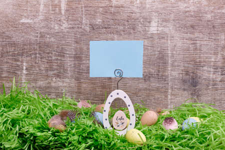 Easter greeting card and colorful quail eggs on a green grass in front of a wooden background. Copy...