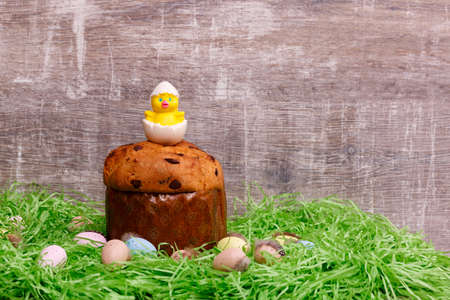 Easter Paska cake and colorful quail eggs in green grass in front of a wooden background....