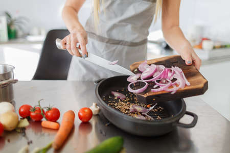 Cooking with vegetables. Female hands are preparing a delicious dish. The process of cutting onions on a wooden board.の写真素材
