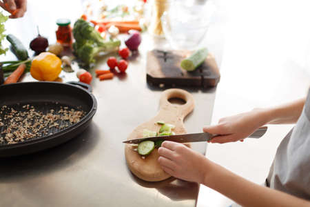 Little hands are cooking a dish from different ingredients. The process of cutting vegetables on a wooden board in a kitchen room.の写真素材
