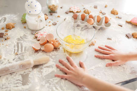 Products for baking cookies, preparation for baking. Children's hands cook sweets. Flour with dough, eggs, eggshells, and biscuits on the kitchen table.の写真素材