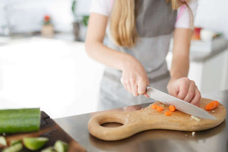A little girl cutting vegetables for the salad on a wooden desk in the kitchen room. Concept of healthy food.の写真素材