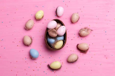 Chocolate Easter eggs, quail eggs and colorful candies on a bright pink background. Easter sweets...