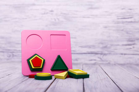 Educational games for children. Red, yellow, pink, blue geometrical figures on the wooden background. Entertaining objects. Close-up. Entertainment concept.の写真素材