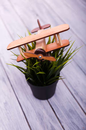 Toys for kids. Childrens toy airplane on the flowerpot with green grass on the wooden gray light background. Close-up. Game concept.の写真素材
