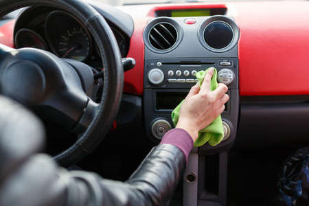 A young woman wipes the dust with a green rag in the car. Dry cleaning of the car panel, car washing.Woman cleaning car dashboard.の写真素材