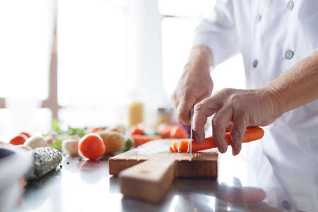 Man's hands with a knife slicing carrots for a dinner on a wooden board. Vegetables full of vitaminsの写真素材
