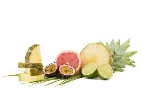 A composition of exotic and tropical fruits with leaves isolated on a white background. A sliced pineapple, lime pieces, halved cut grapefruit and passionfruit.の写真素材