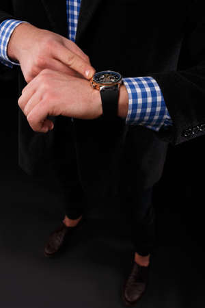 Close-up of a stylish leather black wrist watch on a male hand. A businessman in an elegant costume with a gold watch on a black background.の写真素材