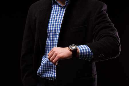 Close-up of a stylish leather black wrist watch on a male hand. A businessman in an elegant costume with a gold watch on a black background.の写真素材